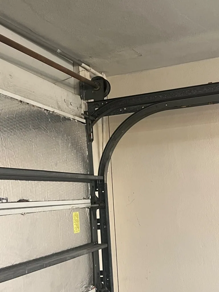 Cable drum, shaft and curved track beside a sectional garage door